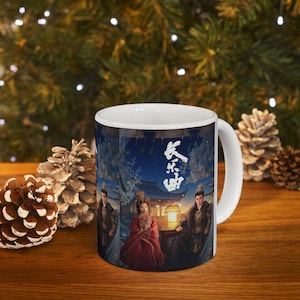 May include: White ceramic mug featuring a colorful illustration of a historical drama scene with three figures in traditional attire. The mug has a curved handle and a glossy finish. The background includes a building and text in Chinese characters.