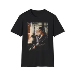 May include: Black t-shirt featuring a framed image of a person in traditional Asian attire. The image shows a person with long hair, seated, and wearing a dark robe. The t-shirt is made of a soft, comfortable material.
