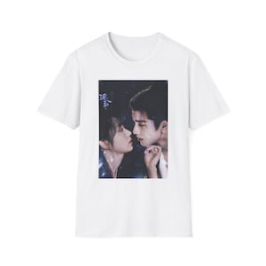 May include: White t-shirt featuring a graphic of a man and woman in a romantic embrace. The image is in a soft, muted color palette. The text in the image is in a foreign language.