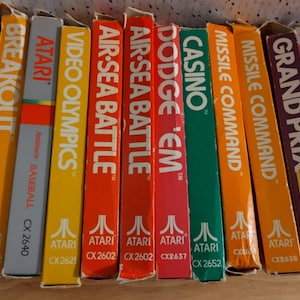 May include: A collection of ten vintage Atari video game cartridges, including Haunted House, Breakout, Video Olympics, Air-Sea Battle, Dodge 'Em, Casino, Missile Command, Grand Prix, and Demon Attack. The cartridges are arranged in a row, with the labels facing the viewer. The cartridges are all in good condition, with no visible damage or wear.