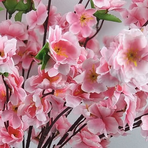 May include: A bouquet of pink artificial cherry blossoms with green leaves. The flowers are arranged on brown branches.