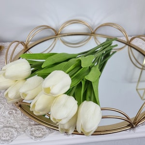 May include: A gold metal tray with a mirrored surface and a scalloped edge. The tray is decorated with a bouquet of white artificial tulips.