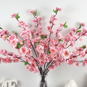 May include: A bouquet of pink artificial cherry blossom branches in a clear glass vase. The branches are arranged in a fan shape and have many small pink flowers.