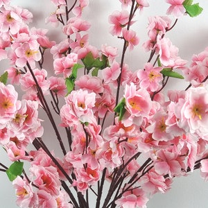 May include: A bouquet of pink artificial cherry blossom branches with green leaves. The branches are arranged in a vase, and the flowers are in full bloom.