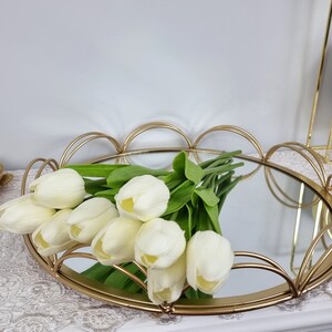 May include: A gold metal tray with a mirrored surface and a scalloped edge. The tray is decorated with a bouquet of white tulips.