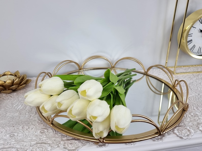 May include: A gold metal tray with a mirrored surface and a scalloped edge. The tray is decorated with a bouquet of white tulips.