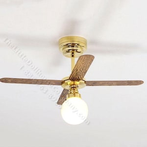 May include: Miniature ceiling fan with three wooden blades and a gold-colored motor housing. The blades have a wood grain pattern. A white globe light hangs below the motor. The fan is mounted on a white ceiling.