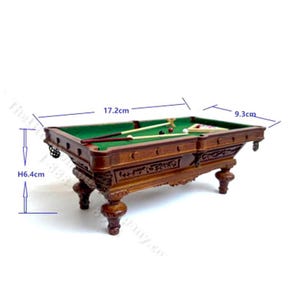 May include: Miniature wooden pool table with green felt, cues, and billiard balls. The table is 6.4 cm high, 17.2 cm long, and 9.3 cm wide. The table has ornate carvings and detailed legs, perfect for a dollhouse or miniature collection.