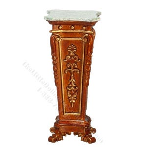 May include: A miniature, ornate pedestal table with a brown finish and gold accents. The top is a light green color. The pedestal has a detailed, carved design. The table is likely for a dollhouse or miniature display.