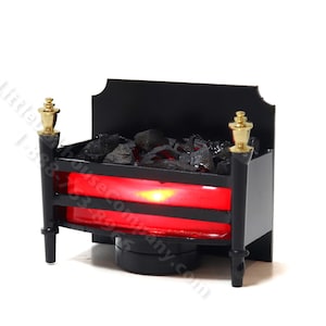 May include: Miniature black fireplace with a red glowing ember effect. The fireplace has gold-coloured accents on the top and is filled with black coal. A decorative piece for a dollhouse or miniature scene.