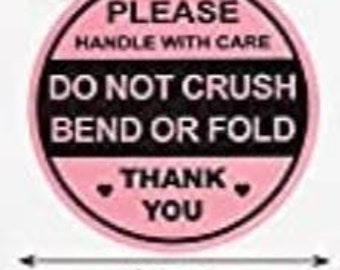May include: A round, pink sticker with black text. The text reads "PLEASE HANDLE WITH CARE DO NOT CRUSH BEND OR FOLD THANK YOU." The sticker is 2 inches in diameter.