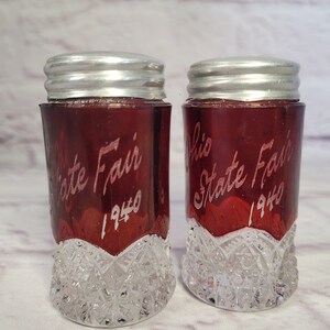 May include: Pair of red glass salt and pepper shakers with silver lids. The shakers are decorated with the text "Ohio State Fair 1940".