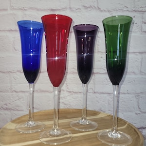 May include: Four stemmed champagne glasses in different colors: blue, red, purple, and green. The glasses are on a wooden tray.