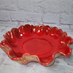 May include: A red ceramic bowl with a wavy edge and gold flecks. The bowl is perfect for serving snacks or holding decorative items.