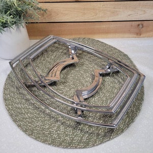 May include: A chrome-plated metal cooling rack with three tiers. The rack is designed to hold hot dishes or cookware.