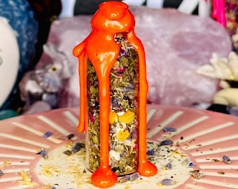 May include: A small glass bottle filled with dried herbs and flowers is sealed with a bright orange wax. The wax drips down the sides of the bottle.