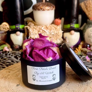 May include: A black cylindrical tin filled with vibrant pink dried rose petals. The label on the front reads: Rose Petals Dried By A Witch, SomethingGnarly Etsy.Com, IG: Wiccanwittchempath, with a tulip illustration on each side of the text.