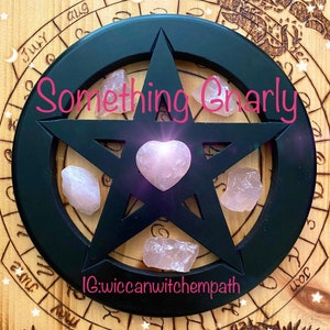 May include: A black wooden pentagram with a pink heart-shaped crystal in the center and four smaller pink crystals at the points of the star. The pentagram is on a wooden background with a circle of zodiac symbols around the edge. The text "Something Gnarly" is written in pink letters above the pentagram. The text "IG:wiccanwitchempath" is written below the pentagram.