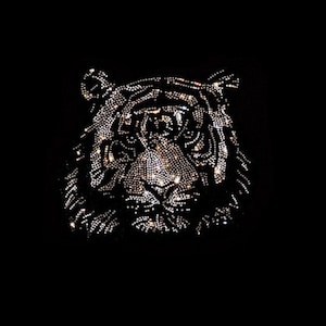 May include: A black background with a tiger's face made of rhinestones. The tiger's face is in the center of the image and is facing forward. The rhinestones are silver and clear.