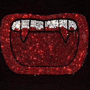 May include: Red rhinestone vampire teeth with fangs, on a black background.