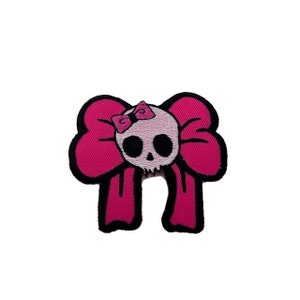 May include: Pink fabric patch with a skull wearing a pink bow. The skull has black eyes and a white face.
