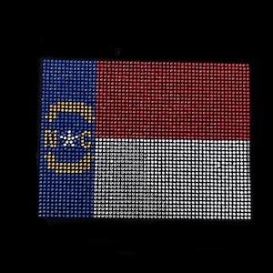 May include: A North Carolina state flag made of rhinestones. The flag is blue, red and white with a yellow star in the centre of a blue circle.
