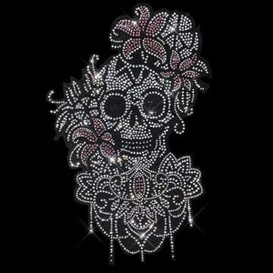 May include: A rhinestone skull with floral embellishments. The skull is surrounded by pink and white flowers and leaves. The skull is outlined in rhinestones and has a detailed design.