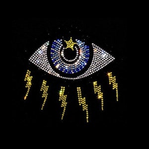 May include: A blue eye with a gold star in the center, surrounded by a ring of clear rhinestones.  The eye is surrounded by a ring of gold lightning bolts.