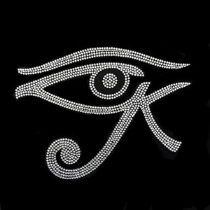 May include: A white rhinestone Eye of Horus symbol on a black background. The eye is detailed with small, sparkling rhinestones, creating a shimmering effect. The symbol is a stylized representation of an eye with a curved eyebrow and a stylized 'K' shape.