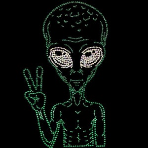 May include: A green alien figure with large eyes and a peace sign hand gesture, created with sparkling embellishments against a black background. The alien's eyes are filled with white embellishments.