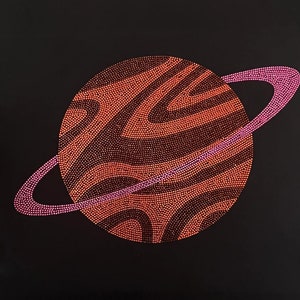 May include: A red and pink planet with rings, made of rhinestones, on a black background.