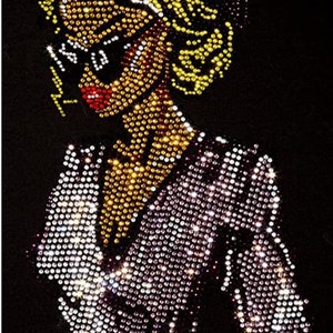 May include: A rhinestone-encrusted image of a woman with blonde hair wearing a sparkly, purple and white dress. The image is on a black background.