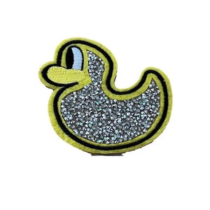 May include: A yellow felt patch with a black outline in the shape of a duck. The duck is covered in silver glitter.