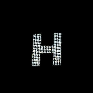 May include: The letter H is made up of small, white, sparkling rhinestones on a black background.