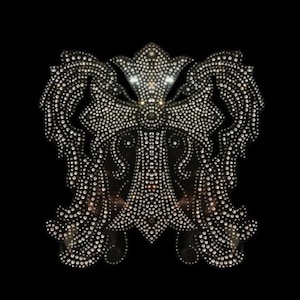 May include: A large, silver, rhinestone cross with intricate details. The cross is surrounded by two wings, also made of rhinestones.