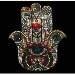 May include: A large, ornate Hamsa hand charm made of rhinestones. The hand is decorated with a blue eye in the center, surrounded by red, gold, and black rhinestones. The Hamsa hand is a symbol of protection and good luck.