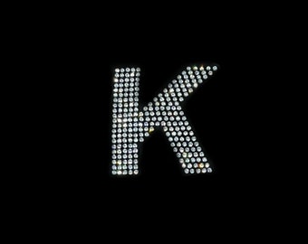 May include: The letter K is formed using small, sparkling, white rhinestones on a black background.