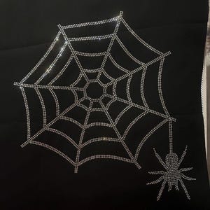 Peut inclure: Un tissu noir avec un grand motif de toile d'araignée en strass argentés et une petite araignée dans le coin inférieur droit.