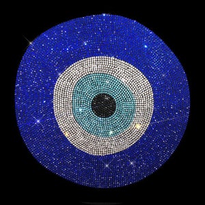 May include: A round, blue, and white decorative item with a central eye design. The eye is composed of concentric circles in shades of blue, white, and black, all encrusted with sparkling rhinestones. The background is black.