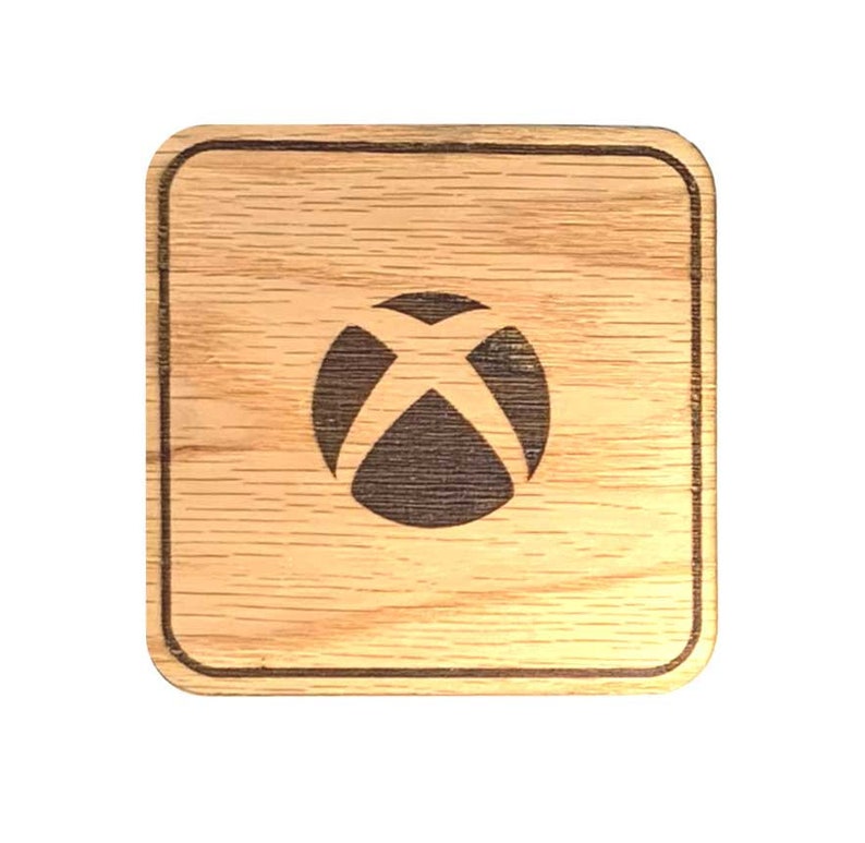 Op de afbeelding: Een houten onderzetter met een donkerbruin Xbox-logo in het midden. De onderzetter is vierkant en heeft een lichtbruine houtnerf.
