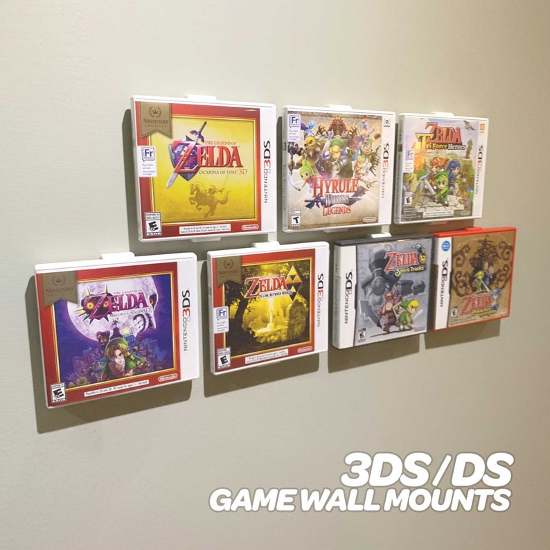 May include: A wall mounted display of video game cartridges for the Nintendo 3DS and DS consoles. The cartridges are displayed in white plastic holders with the game titles visible. The text "3DS/DS GAME WALL MOUNTS" is printed below the display.