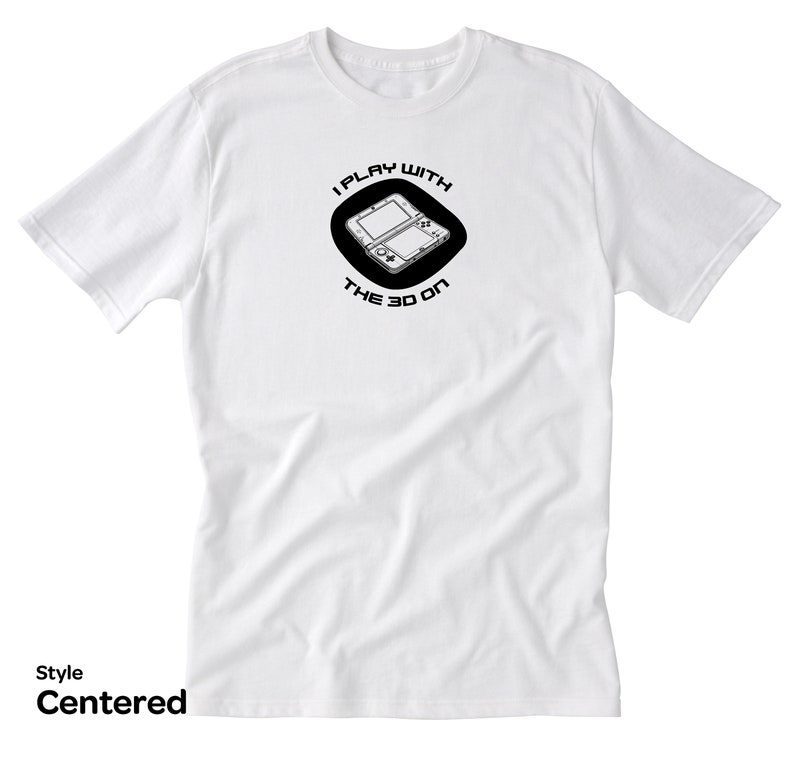 May include: White t-shirt with a black circle graphic featuring a Nintendo 3DS handheld gaming console and the text "I play with the 3D on".