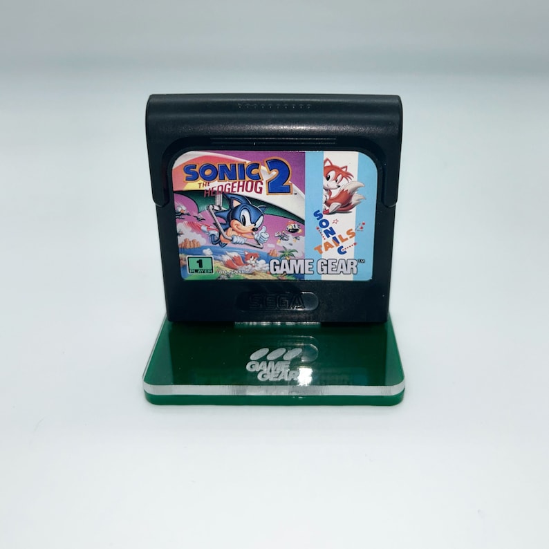 May include: A green acrylic stand with the words "Game Gear" printed on it. A black Sega Game Gear console is on the stand. The console is displaying the game "Sonic the Hedgehog 2".