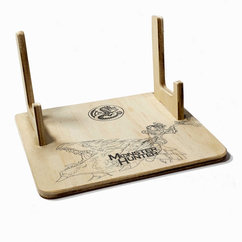 May include: A wooden stand with a Monster Hunter logo and a dragon design. The stand has two upright supports for displaying items.