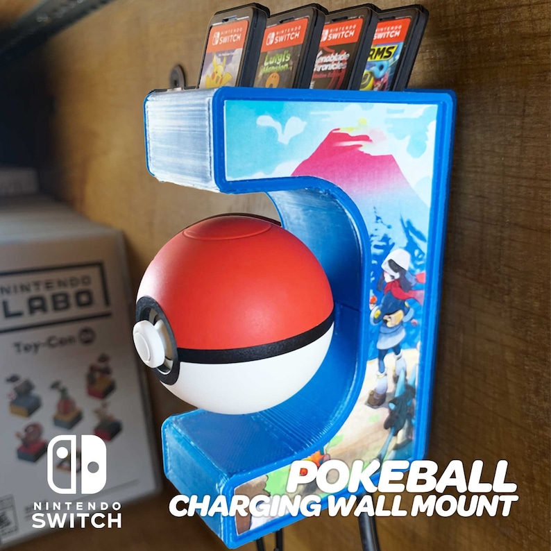 May include: A blue and red Pokeball-shaped wall mount for charging a Nintendo Switch console. The mount has a slot for game cartridges and a Pokeball design. The text "POKEBALL CHARGING WALL MOUNT" is printed on the front of the mount.