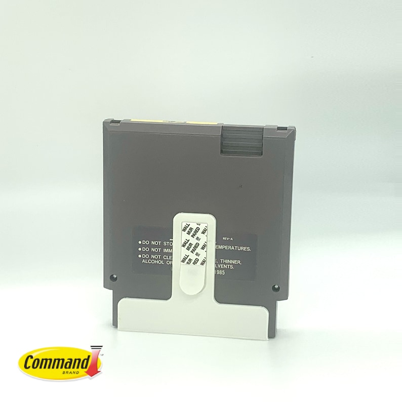 May include: A grey Nintendo Entertainment System (NES) game cartridge with a white label. The label has text that reads "DO NOT STORE", "DO NOT IMMERSE", "DO NOT CLEAN", "ALCOHOL OR", "REV-A", "TEMPERATURES", "THINNER", "SOLVENTS", and "1985".