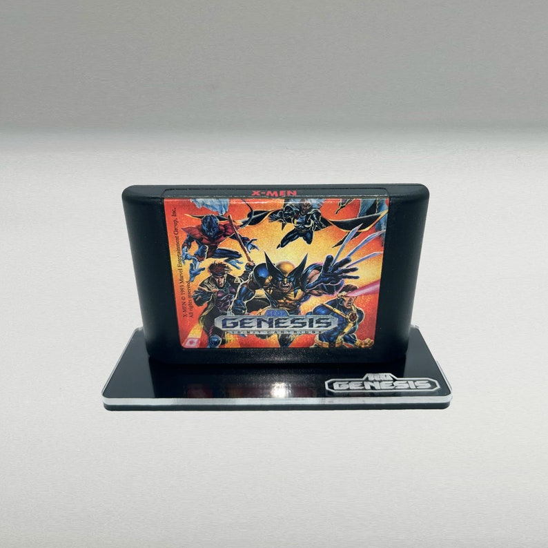 Op de afbeelding: Een zwarte Sega Genesis-spelcartridge met een kleurrijk label waarop de X-Men-personages te zien zijn. Het label heeft de titel "X-Men" en het Sega Genesis-logo. De cartridge staat op een transparante acrylstandaard met het Sega Genesis-logo.