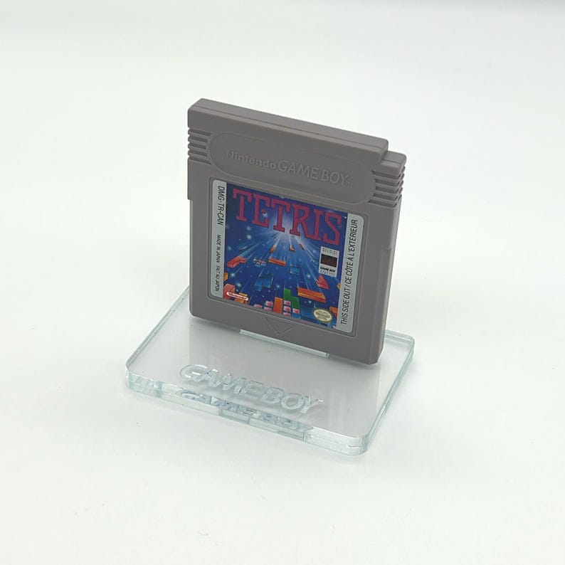 May include: A gray Game Boy cartridge for the game Tetris is displayed on a clear acrylic stand. The stand has the word "GAMEBOY" engraved on it.
