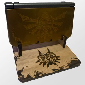 May include: A wooden stand with a carved Majora's Mask design, holding a gold Nintendo Switch console with a Triforce design on the back.