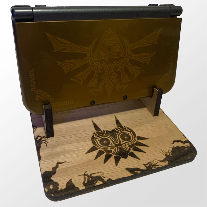 May include: A wooden stand with a carved Majora's Mask design, holding a gold Nintendo Switch console with a Triforce design on the back.